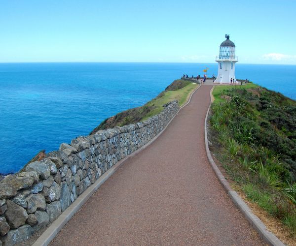 A white lighthouse on a peak overlooking a blue ocean